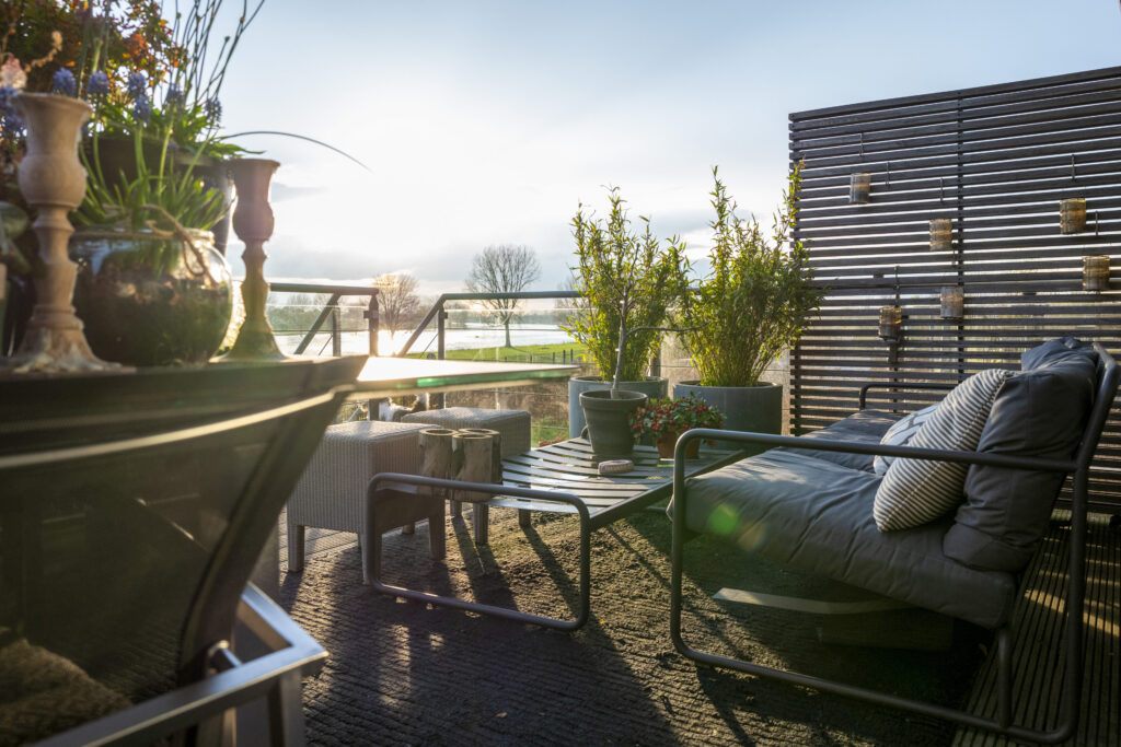 Ausblick von Holzterrasse mit Möbeln vom Sonnenlicht beschienen.