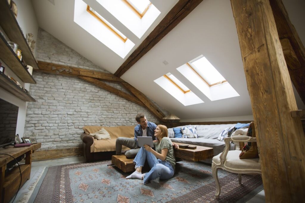 Glückliches junges Paar sitzt zu Hause auf dem Boden im Wohnzimmer mit Dachschräge