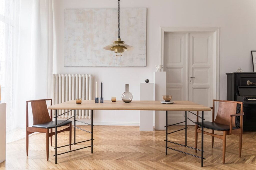 Stilvolles und modernes Esszimmer mit Designer-Tisch, Stühlen, goldener Pendelleuchte, abstrakten Gemälden und eleganten Accessoires. Tropische Blätter in einer Vase. Eklektische Wohnkultur.