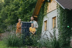 Eine dreiköpfige Familie steht im Garten ihres Haus und hält ein Solarpanel in der Hand