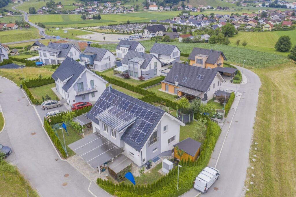 Diese Luftaufnahme zeigt Häuser in einem Vorstadtviertel, eingebettet in die natürliche Schönheit der Landschaft. Viele Häuser sind mit Solaranlagen auf den Dächern ausgestattet und verbinden so Technologie mit Natur.