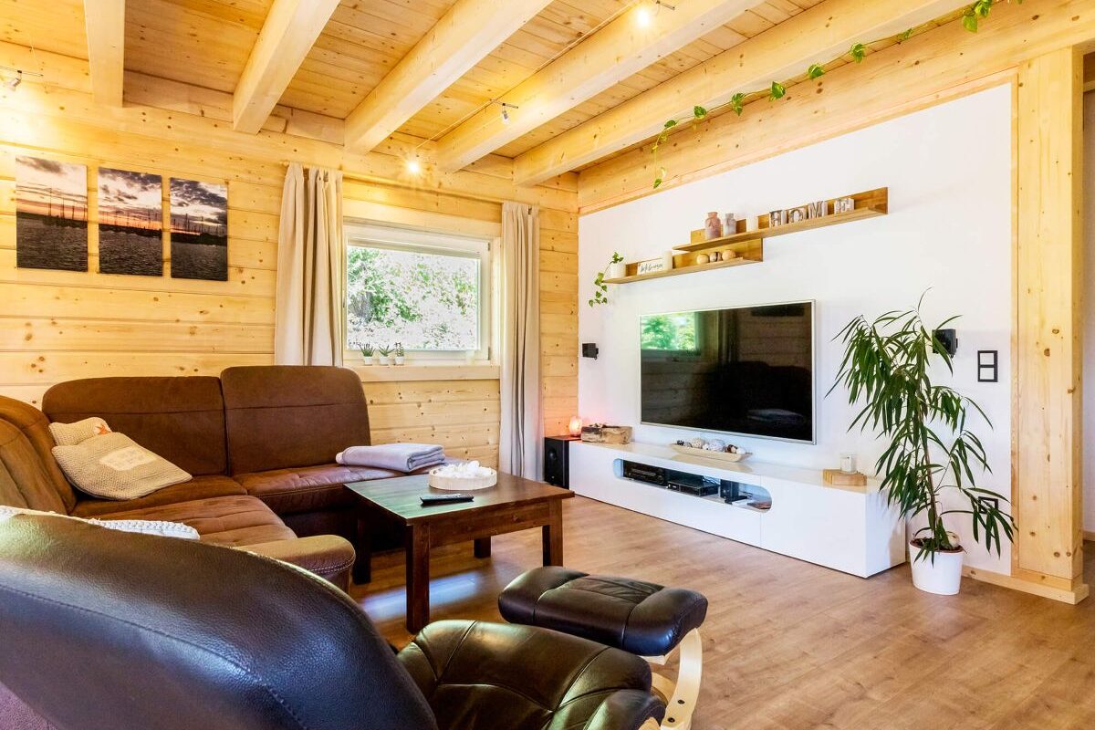 Blockhaus Aalborg Wohnzimmer in Holzhaus mit dunklen Ledermöbeln und weißer Wand mit TV