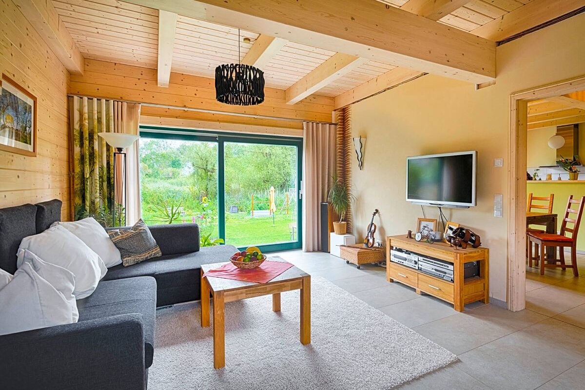 Blockhaus Alpina One Wohnzimmer mit Holzdecke und dunklem Sofa